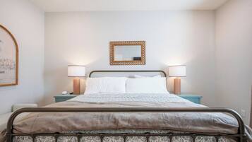 A bed with a metal frame, two bedside lamps, a mirror above the bed, and a wall-mounted picture frame.
