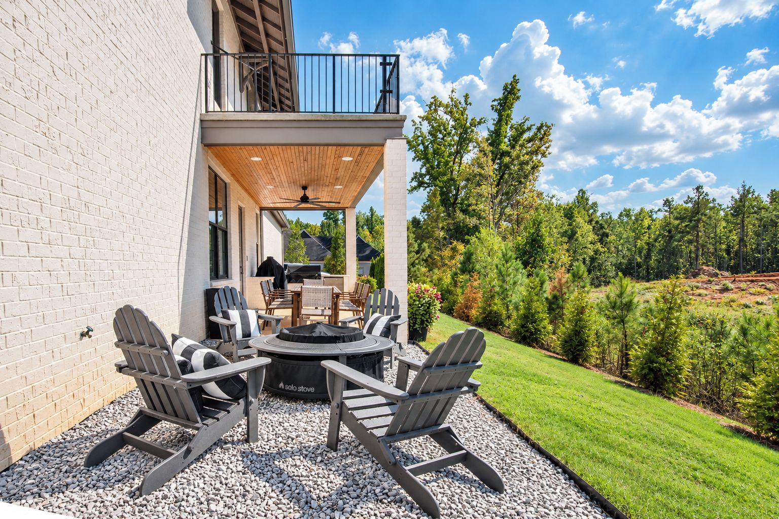 An outdoor patio with a round table and chairs, a grill, and a view of a forested area.