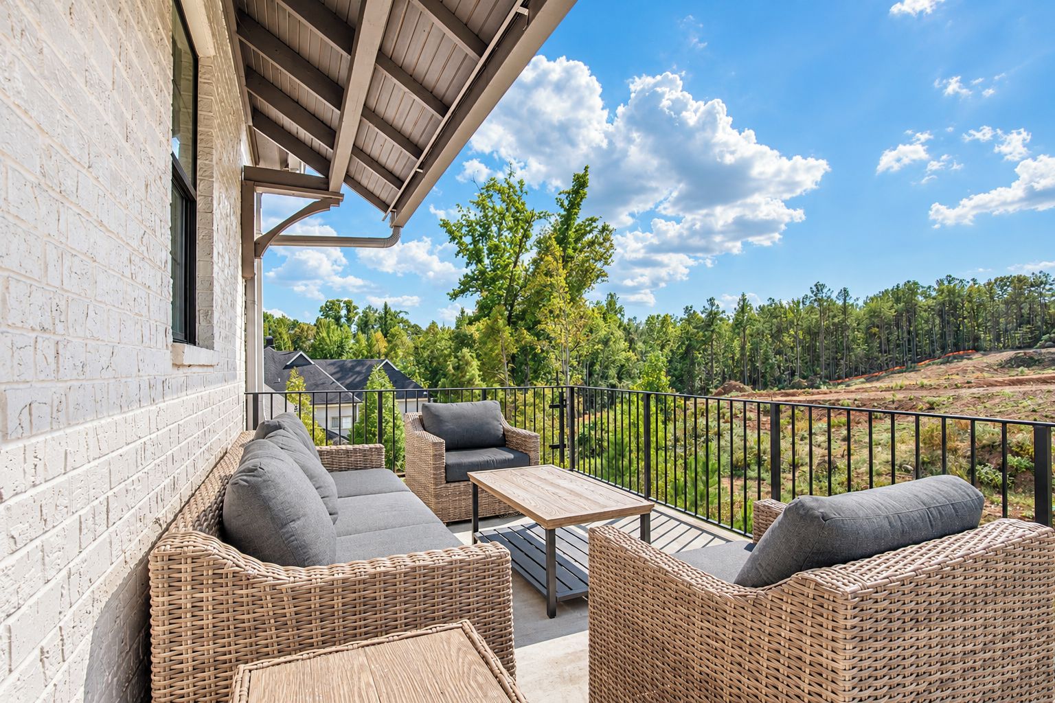 An outdoor patio with wicker furniture, a table, and a view of a forested landscape.