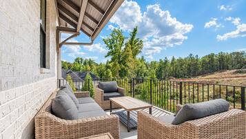 An outdoor patio with wicker furniture, a table, and a view of a forested landscape.