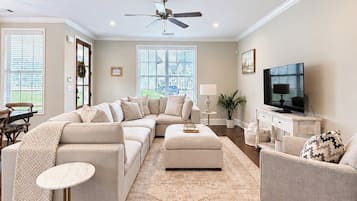 Una sala de estar con sofá modular, reposapiés, mesa de centro, mueble para televisión y ventilador de techo.