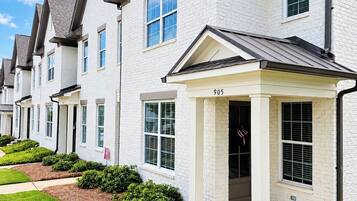 A row of modern townhouses with a uniform architectural style, featuring white brick exteriors, dark roofs, and a central entrance with a covered porch.
