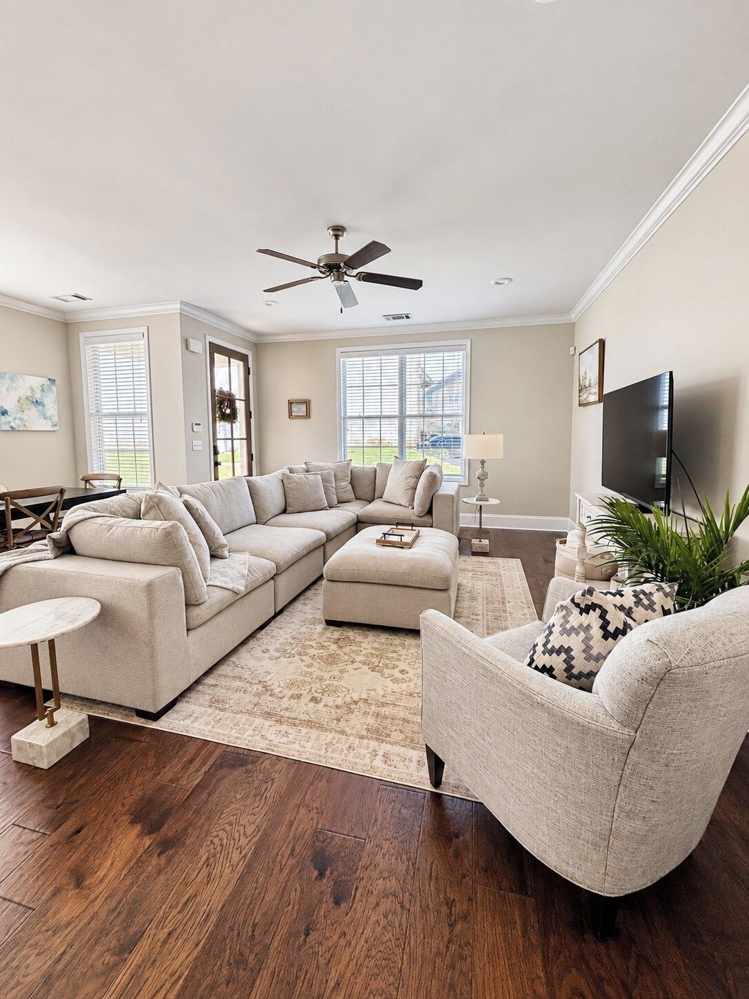A living room with a sectional sofa, a round coffee table, a side chair, a television, and a ceiling fan.