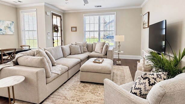Ein Wohnzimmer mit Ecksofa, rundem Couchtisch, Sessel, Fernseher und Deckenventilator.