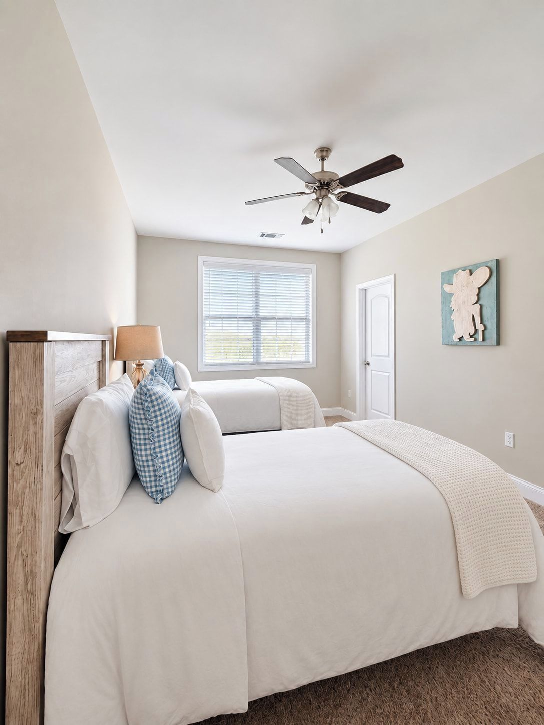 A bedroom with a bed, a ceiling fan, a window with blinds, a door, and a wall-mounted artwork.