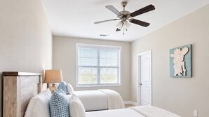 Ein Schlafzimmer mit einem Bett, einem Deckenventilator, einem Fenster mit Jalousien, einer Tür und einem an der Wand hängenden Kunstwerk.