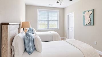 A bedroom with a bed, a ceiling fan, a window with blinds, a door, and a wall-mounted artwork.