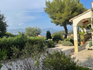 Ein gepflasterter Weg führt zu einer überdachten Außenbereits mit Blick auf Berge und Meer.