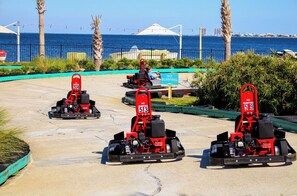 Drei Go-Karts auf einer Asphaltstrecke, ein Schild mit der Aufschrift 'Kein Rammen', Palmen und im Hintergrund der Blick auf das Meer.