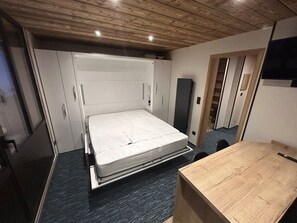 Ein kleines Zimmer mit einem Bett, einem Schreibtisch und einem Kleiderschrank.