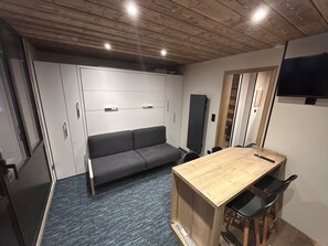 Ein gemütlicher Raum mit einer Couch, einem kleinen Holztisch und einem an der Wand befestigten Fernseher.