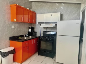 Eine kleine Küche mit einem Gasherd, einem weißen Kühlschrank und orangenen Schränken.