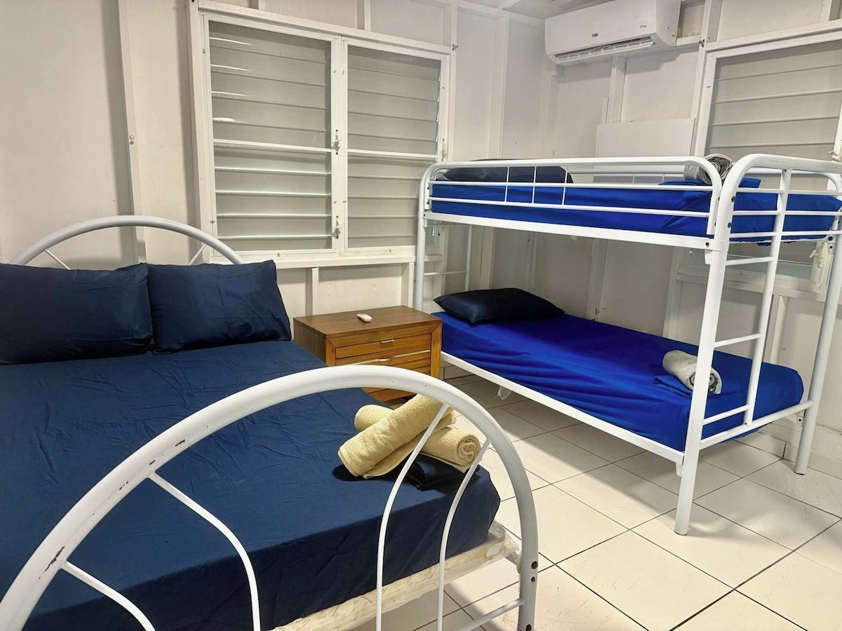 A room with bunk beds, a single bed, a wooden nightstand, and a window with blinds.