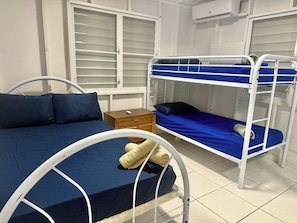 A room with bunk beds, a single bed, a wooden nightstand, and a window with blinds. - Vibrant Retreat | Poolside Fun Minutes from Beach (Cabo Rojo)