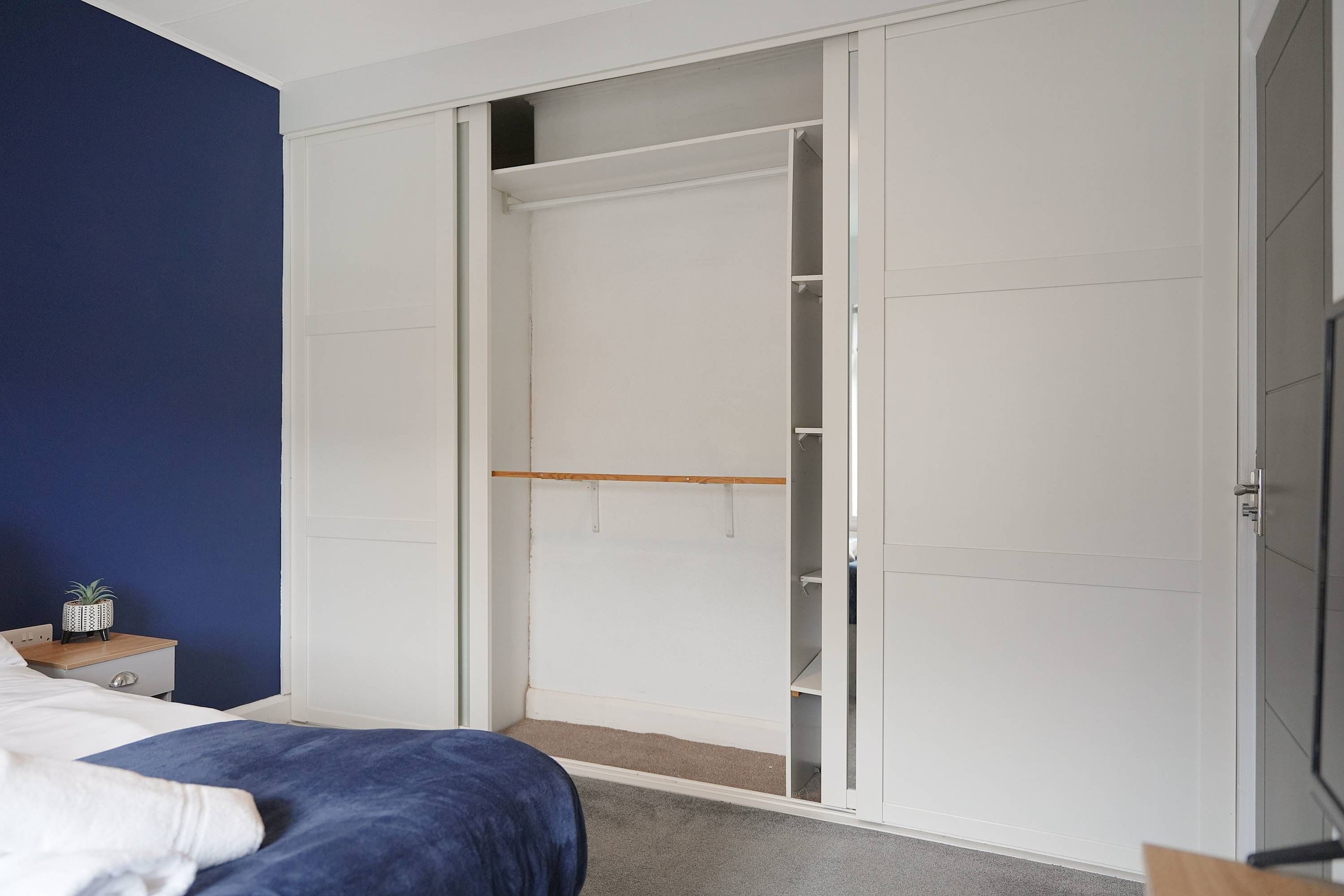 Una camera da letto con un letto, un comodino, una parete blu e un armadio bianco con un appendiabiti.