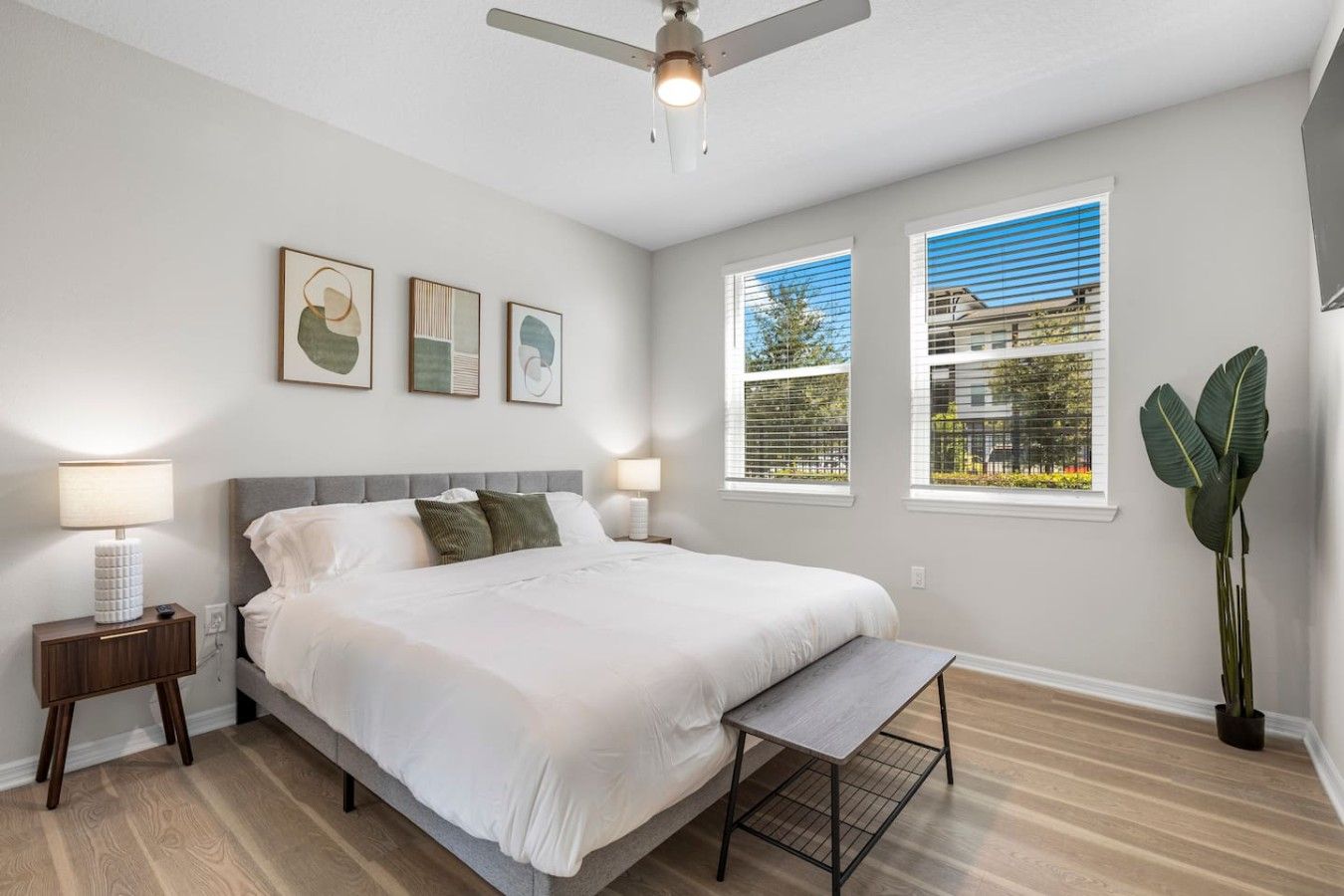 A bedroom with a bed, bedside lamps, a ceiling fan, and two windows with blinds.