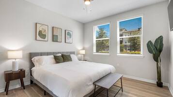 A bedroom with a bed, bedside lamps, a ceiling fan, and two windows with blinds.