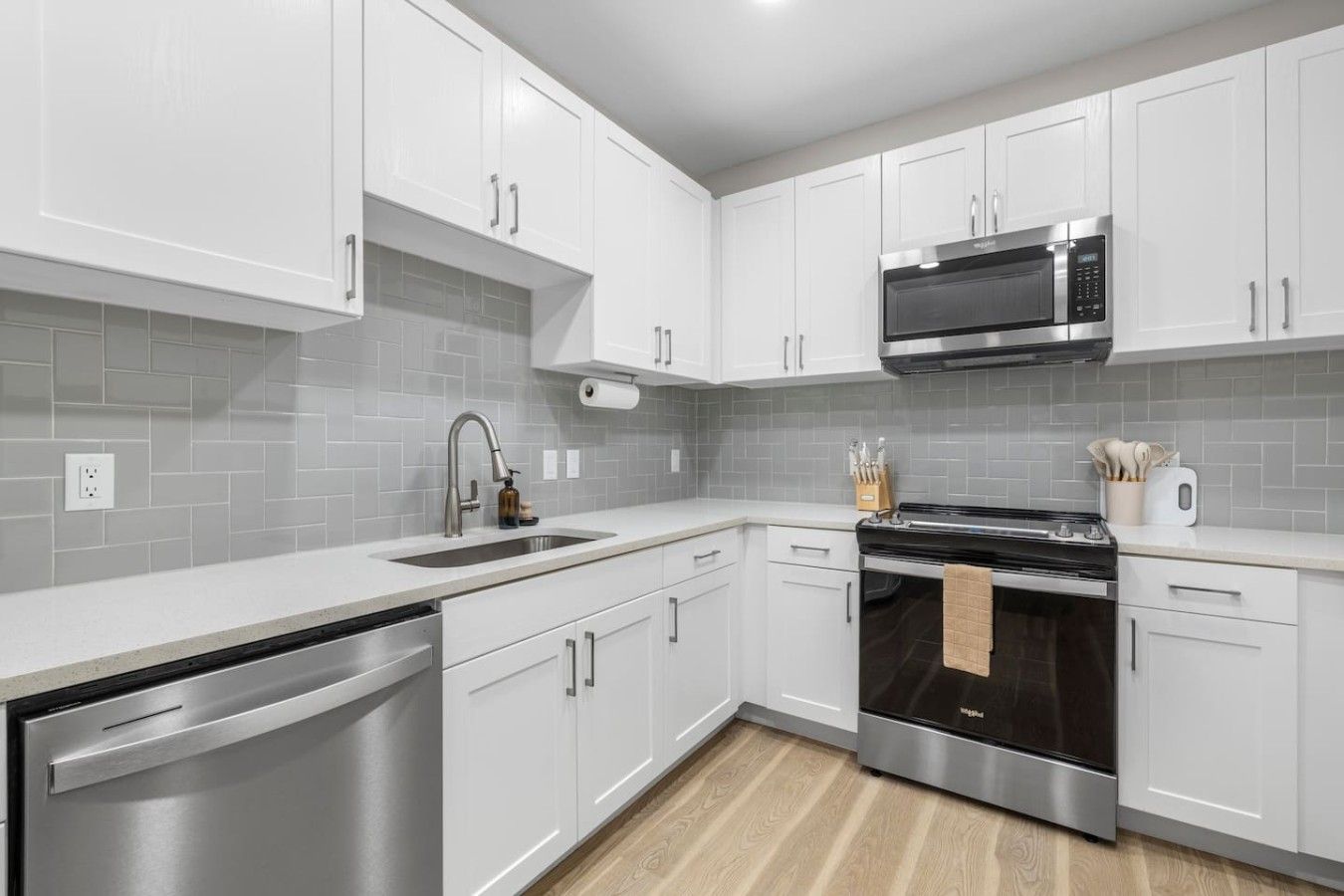 A modern kitchen with white cabinets, a stainless steel dishwasher, a black stove, and a microwave.