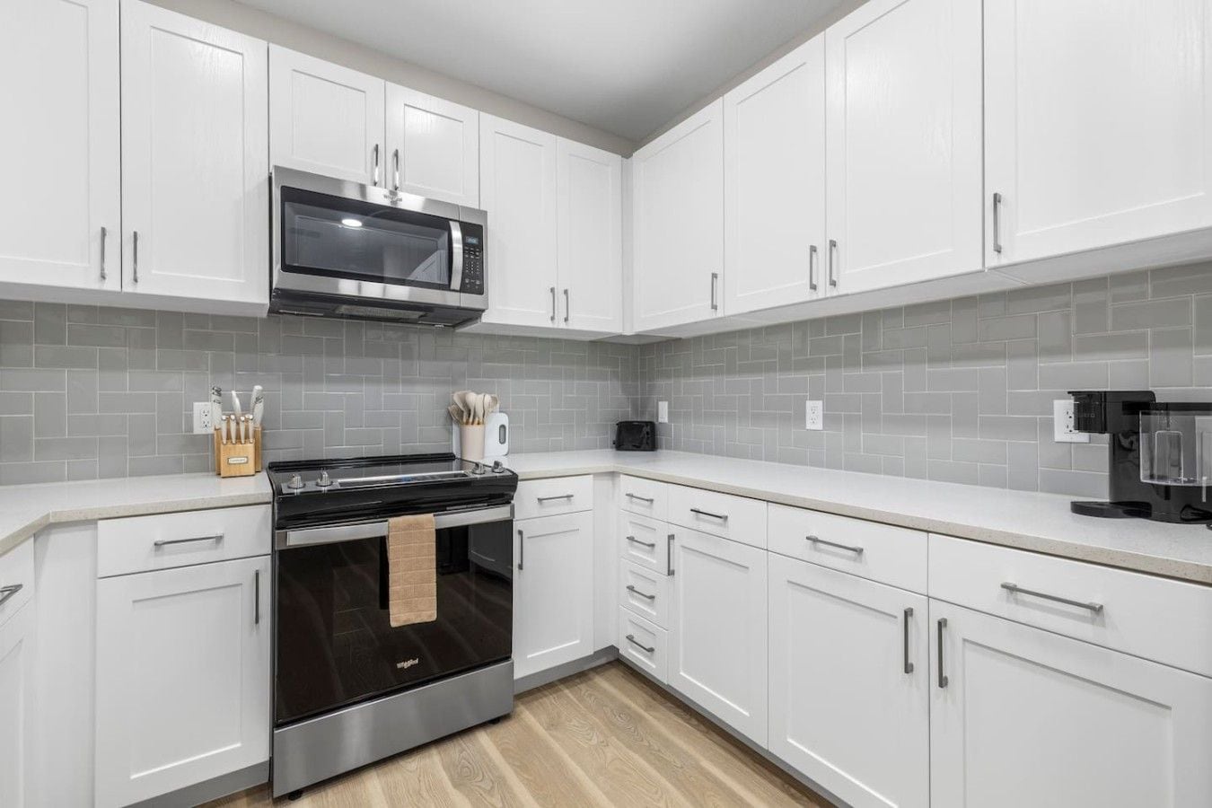 A modern kitchen with white cabinets, a stainless steel oven, and a microwave.