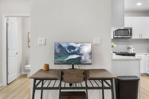 Een moderne keuken met witte kasten, een magnetron en een eethoek met tafel en stoelen.