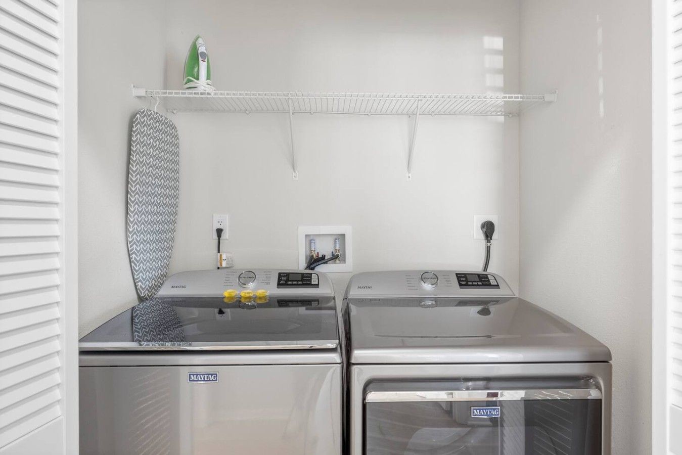 Une buanderie équipée de deux machines à laver Maytag, d’un étendoir et d’un fer à repasser vert posé sur une étagère.