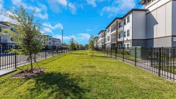 A residential area with a well-maintained lawn, a black metal fence, and multi-story apartment buildings.