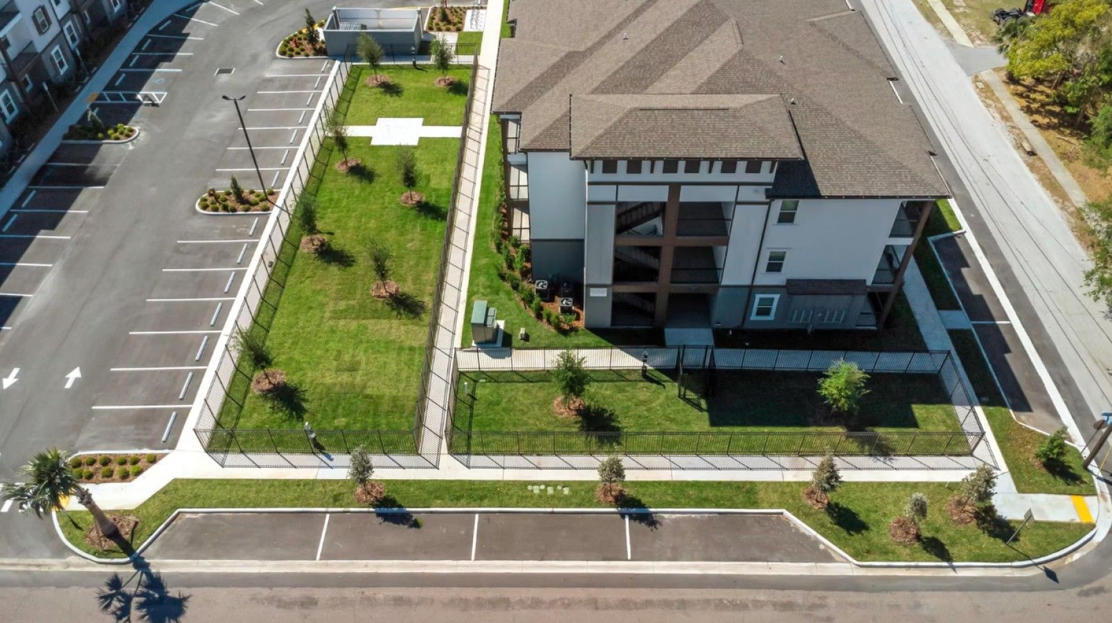 An aerial view of a modern building with a parking lot, a grassy area with trees, and a clear sky.