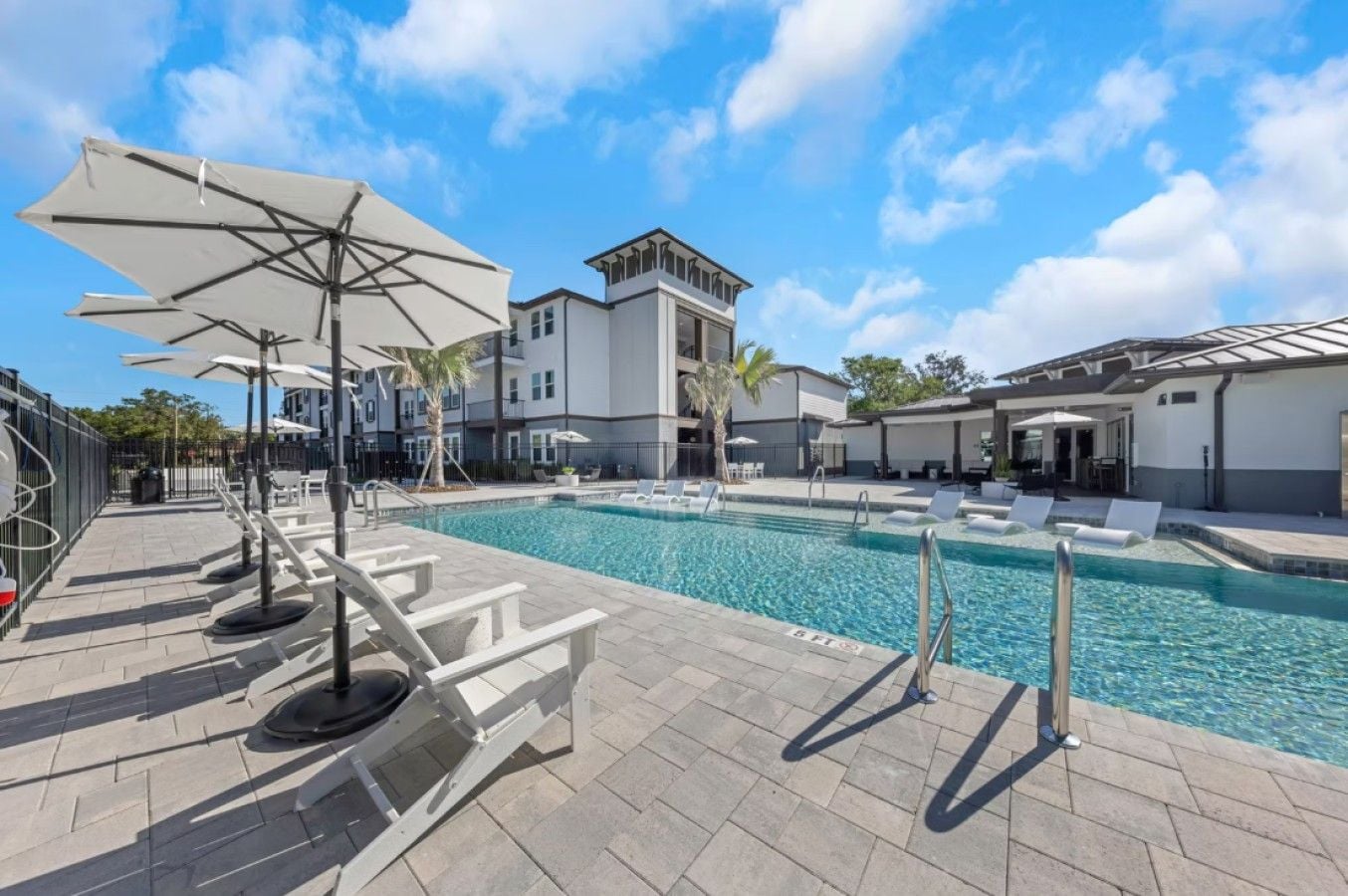 Une piscine entourée de chaises longues et de parasols, le tout bordé d’un bâtiment au design moderne.
