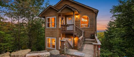 A two-story wooden cabin with a balcony, a staircase, and a porch.