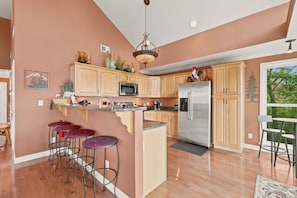 A kitchen with wooden cabinets, a stainless steel refrigerator, a microwave, and a bar area with stools. - Cedar Sunset - Big Views, Two Fireplaces, 4BR on Beech Mountain (Beech Mountain)