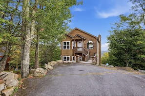 A two-story wooden cabin with a porch, a staircase, and a view of the surrounding forest. - Cedar Sunset - Big Views, Two Fireplaces, 4BR on Beech Mountain (Beech Mountain)