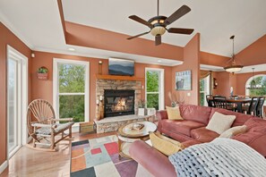 A living room with a fireplace, a sofa, a rocking chair, and a dining area with a table and chairs. - Cedar Sunset - Big Views, Two Fireplaces, 4BR on Beech Mountain (Beech Mountain)