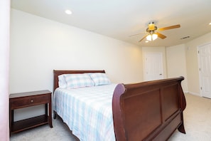 Quarto com cama de madeira, mesa de cabeceira, ventilador de teto e paredes brancas.