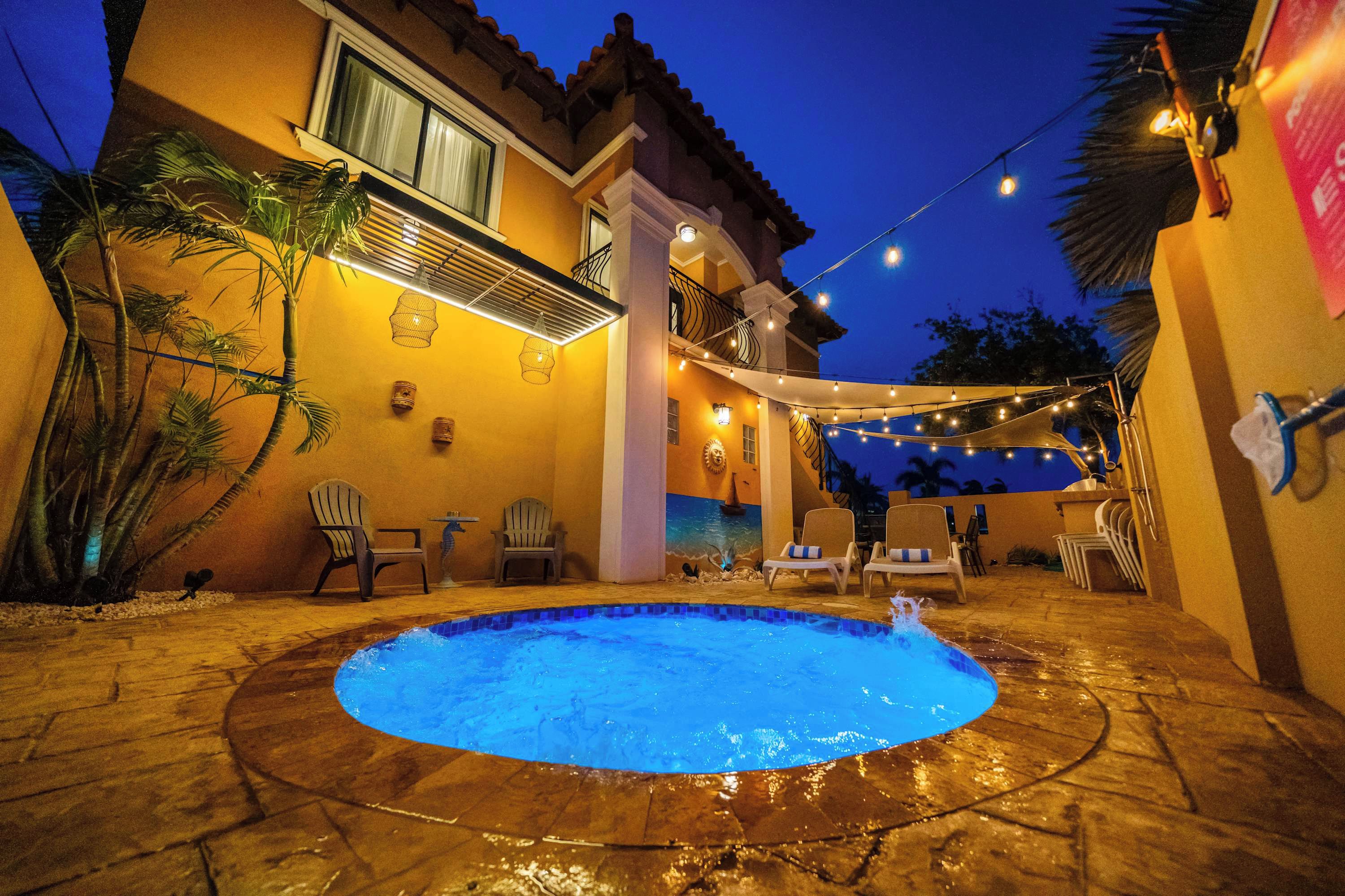 Una piscina con sillones de descanso e iluminación colgante en un patio trasero.