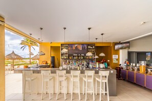 Eine Bar mit einer langen Theke, mehreren Barhocker und einer Auswahl an Flaschen und Gläsern.