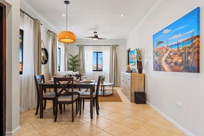 A dining area with a table set for four, a ceiling fan, and a painting on the wall. - Villa Sail Away | Private Jacuzzi & Courtyard (Noord)