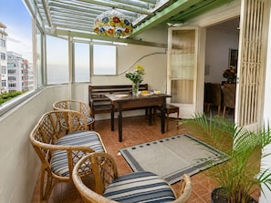 Un balcón con mobiliario de mimbre, una mesa de comedor y una planta en maceta.