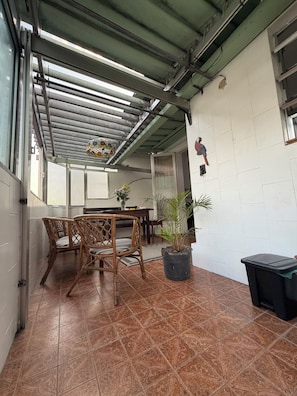 Un espacio al aire libre cubierto con una mesa, sillas, una planta en maceta y un basurero.