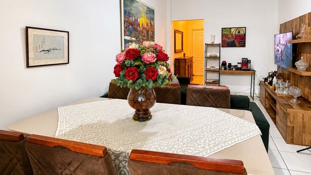 Un coin repas avec une table ronde, des chaises à revêtement marron, un vase de fleurs et des œuvres d’art accrochées aux murs.