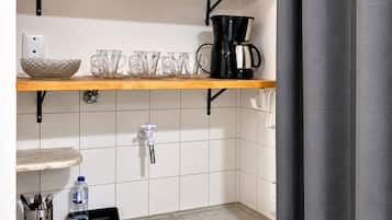 Ein Badezimmer mit Waschbecken, einer Kaffeemaschine und einem Regal mit Tassen und einer Schüssel.
