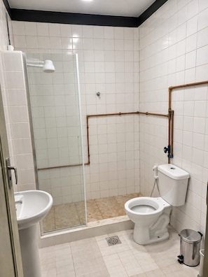 Casa de banho com chuveiro, sanita, lavatório e um contentor de lixo.