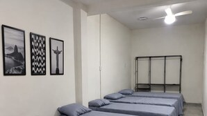 A hotel room with four beds arranged in a row, a ceiling fan, and three framed pictures on the wall. - Hospedagem Rio Lapa 3 (Rio de Janeiro)