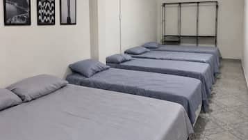 Ein Hotelzimmer mit vier nebeneinander stehenden Betten, einem Deckenventilator und drei gerahmten Bildern an der Wand.