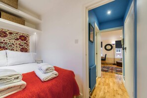 A hotel room with a bed, a red blanket, and a hallway leading to another room. - Cosy 1-bed - Fitzrovia - Sleeps 3 (London)