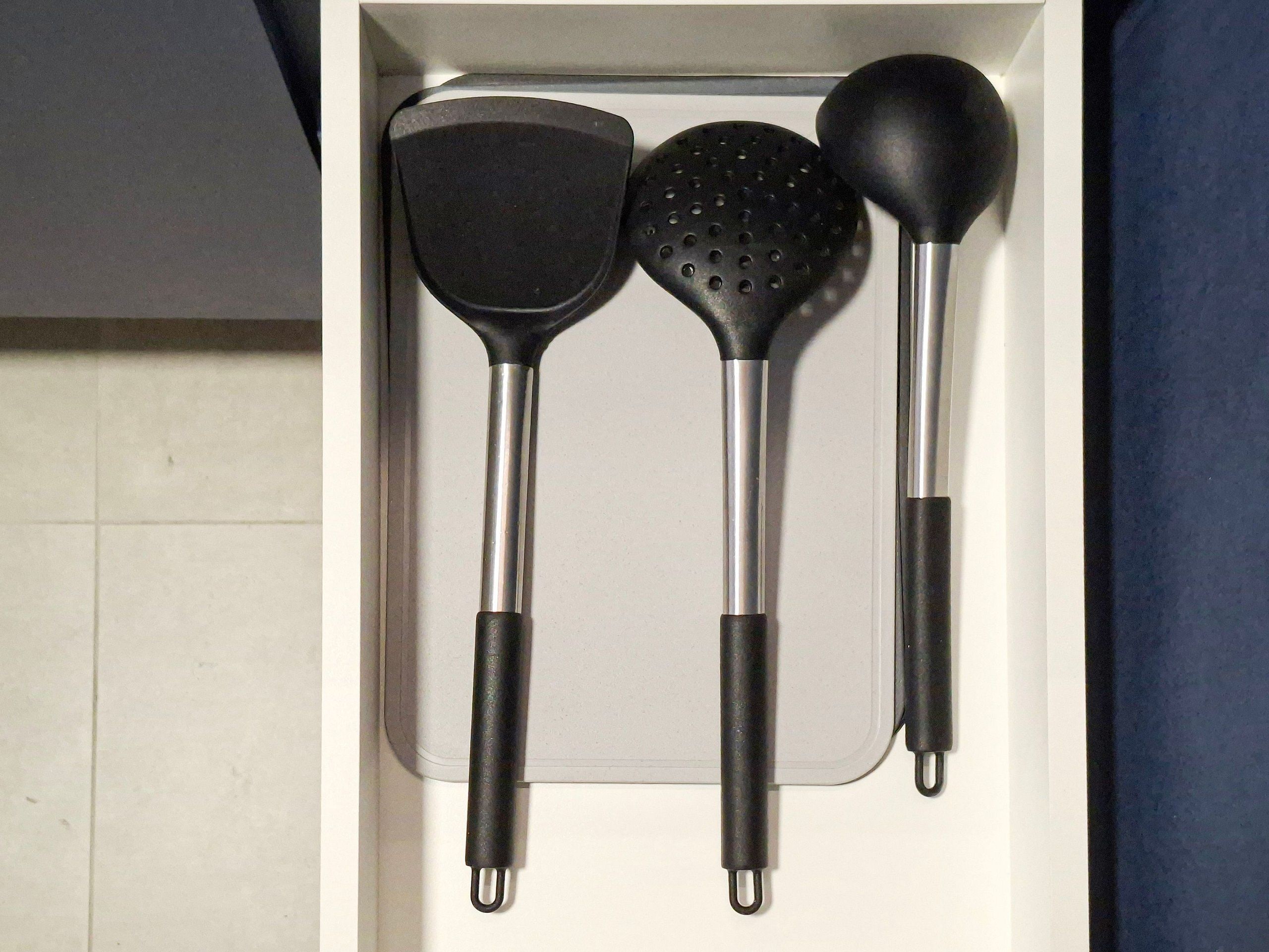 Un cajón con tres utensilios de cocina: una espátula, una cuchara escurridora y una cuchara grande.