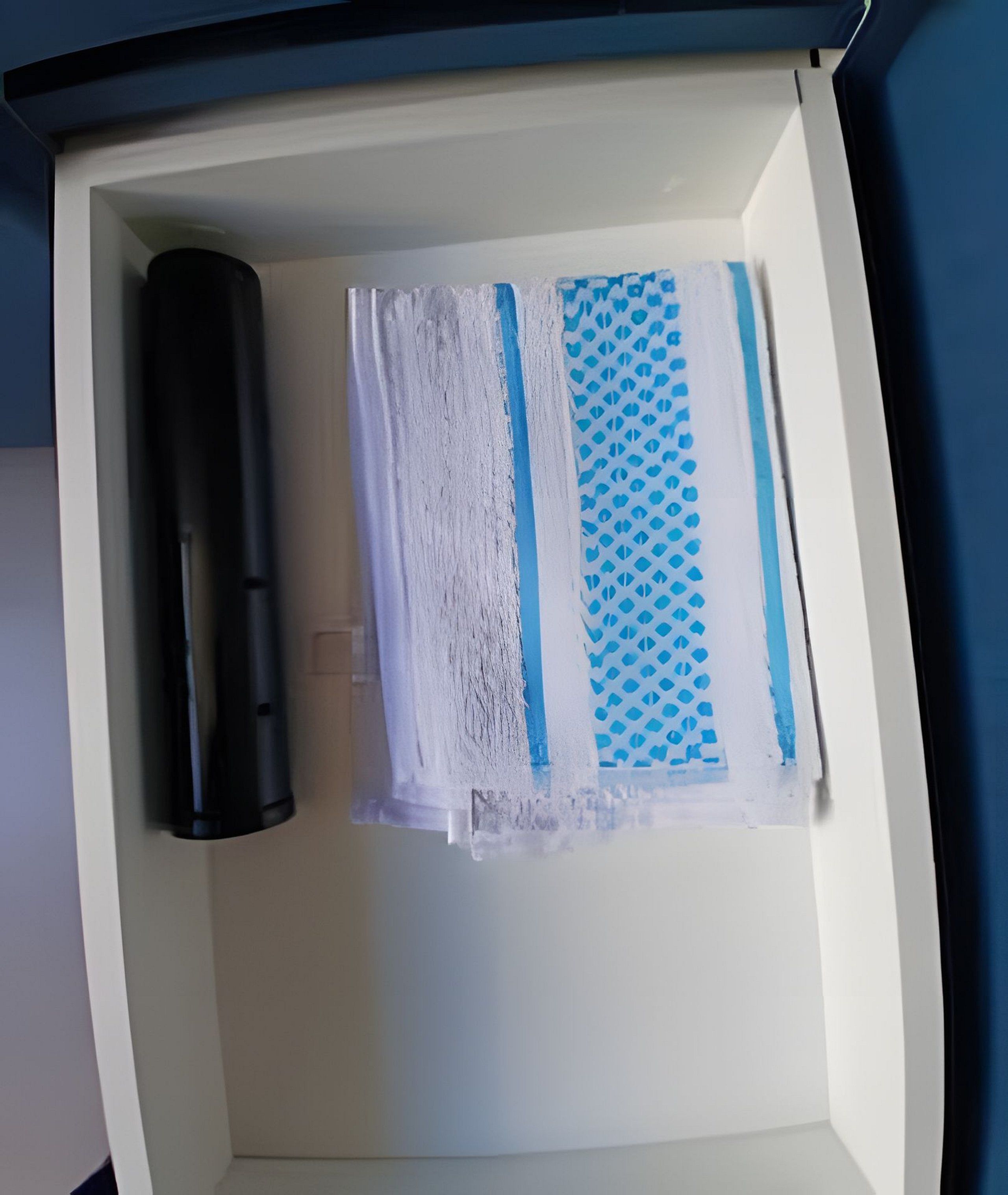 A drawer with a black cylindrical object, a white object with blue patterns, and a blue patterned object.