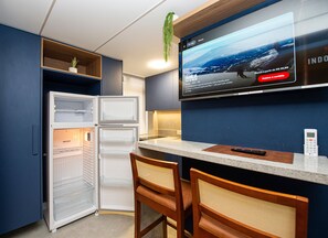 A compact kitchen with a built-in refrigerator, a microwave, and a flat-screen TV mounted on the wall. - SHB - Studio Grego com Pé na Areia (Santos)
