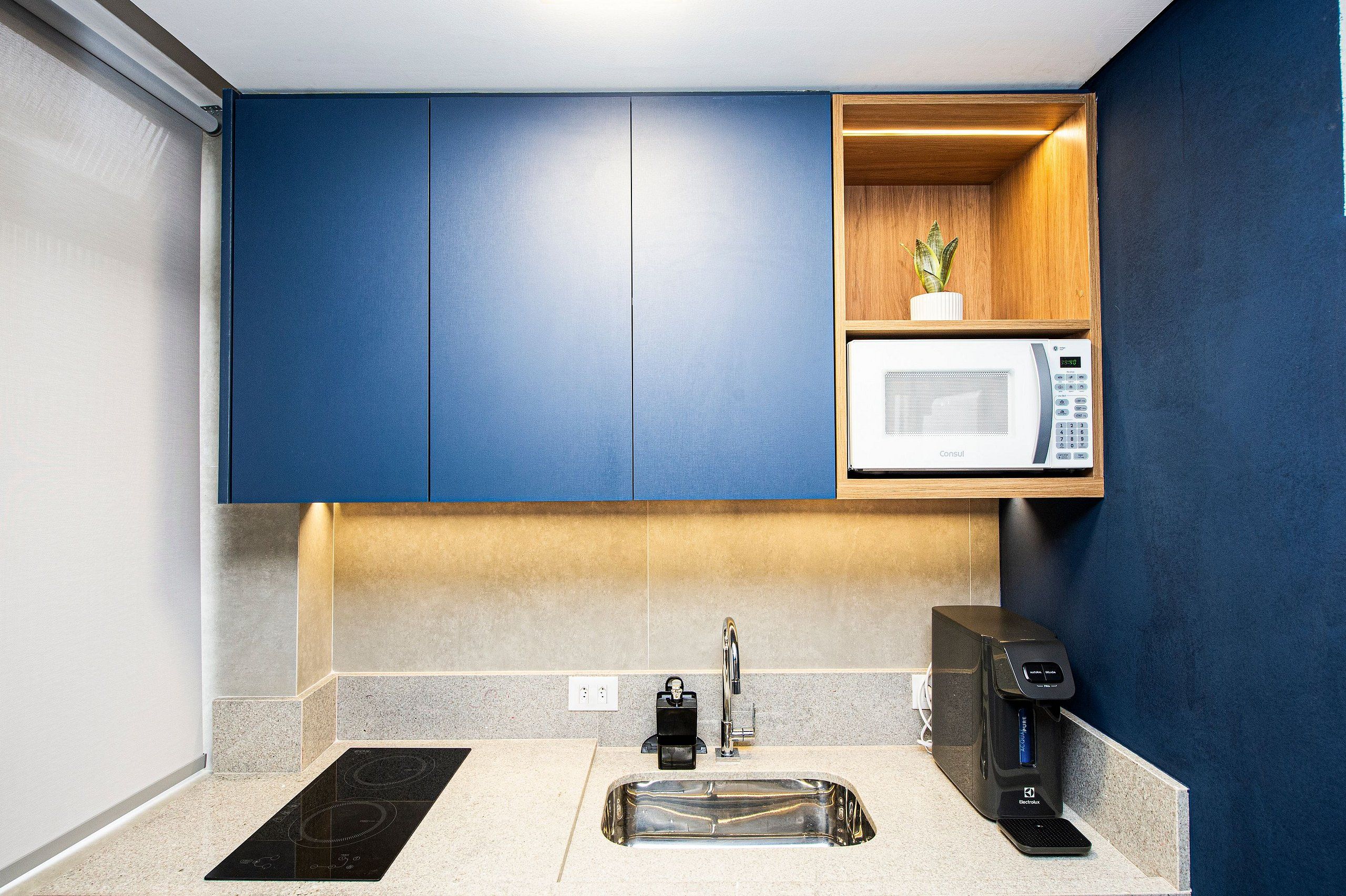 A modern kitchen with a built-in microwave, coffee machine, and a small shelf with a plant.