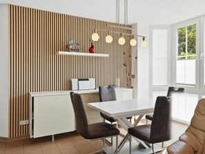 Ein stilvoller Essbereich mit einem weißen Tisch, dunklen Stühlen, einer Wand aus Holzlamellen und Pendelleuchten.