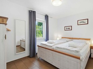 Ein Schlafzimmer mit einem Bett, einem Spiegel, einem Fenster mit Vorhängen und einer Wand mit zwei gerahmten Bildern.